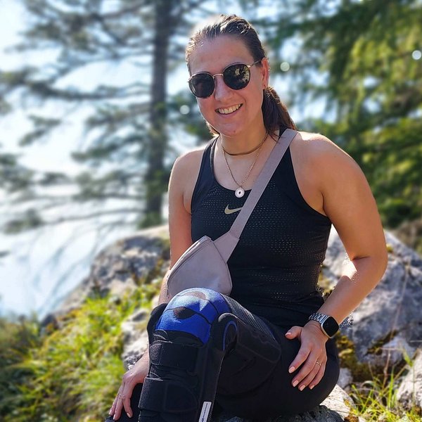 Das Bild zeigt Kniepatientin Katrin mit ihrer Bauerfeind-Orthese SofTec Genu im Wald bei einer Wanderpause.